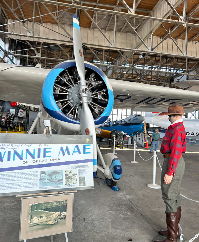 One of the most historically significant civilian aircraft at Hangar B is an exact full-scale model of the Lockheed Vega “Winnie Mae”, which commemorates the first solo flight around the world by Wiley Post, who circumnavigated the globe and returned to Floyd Bennett Field in 7 days, 18 hours, 49 minutes on July 22, 1933