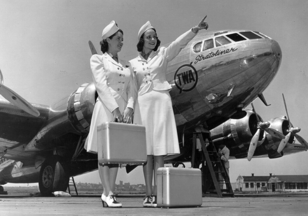 On the Runway - Flying In Fashion New York Airport TWA Stewardesses in front of Boeing 307 Stratoliner with Mechanic Working on Engine at LaGuardia Airport